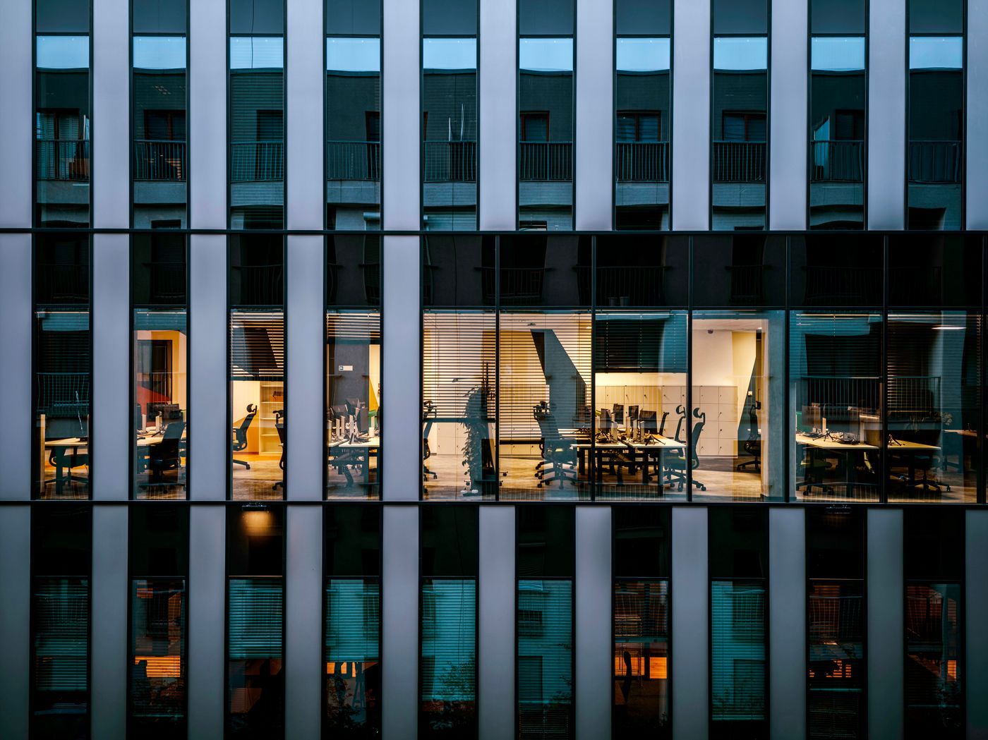 Façade vitrée d'un édifice à bureaux, bureaux éclairés en fin de journée
